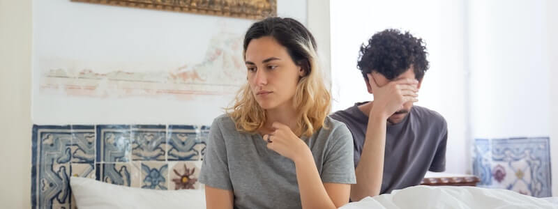 זוג יושבים על המיטה עם מבטים של מבוכה ואכזבה עקב חרדת ביצוע.