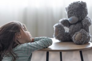 ילדה מסתכלת על בובת דובי בעצבות